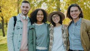 Four friends smiling together in a park during a sunny fall day.